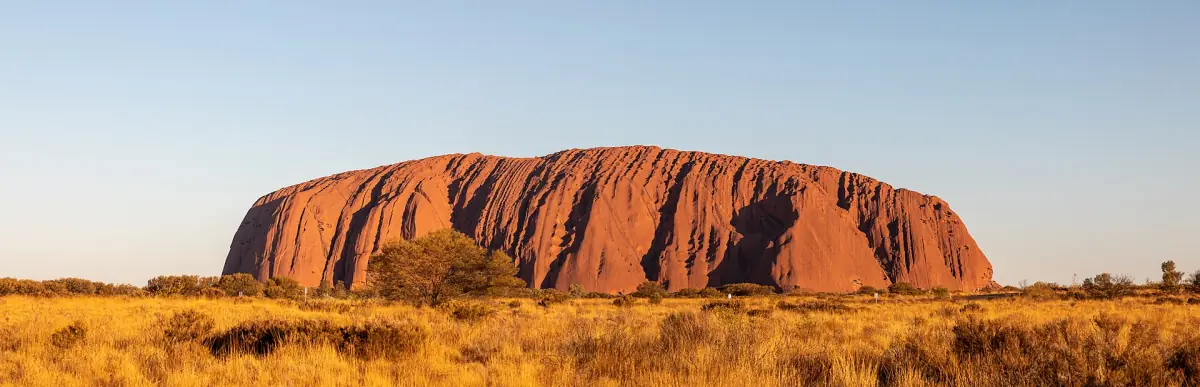 Uluru glowing red at sunset above the plain